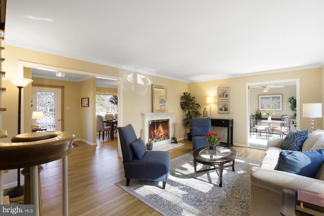 living room with a lit fireplace, light wood-style flooring, and crown molding