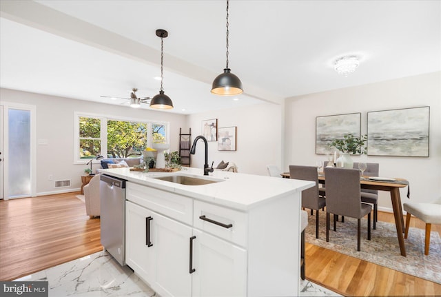 kitchen with an island with sink, sink, pendant lighting, stainless steel dishwasher, and white cabinetry