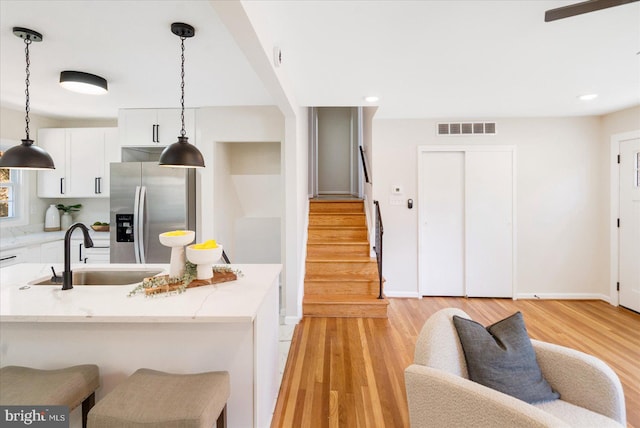 kitchen featuring white cabinets, light stone counters, light hardwood / wood-style flooring, stainless steel refrigerator with ice dispenser, and sink