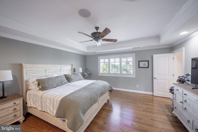 bedroom featuring dark hardwood / wood-style floors, ceiling fan, ornamental molding, and a tray ceiling