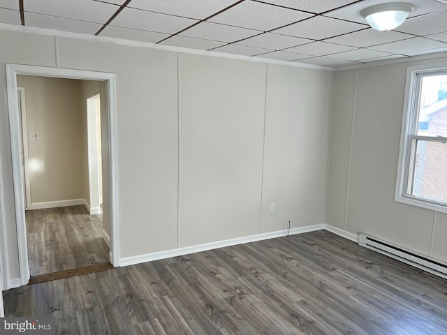 empty room with a drop ceiling, dark hardwood / wood-style floors, and a baseboard radiator