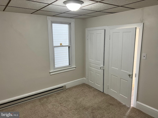 unfurnished bedroom with a drop ceiling, baseboard heating, and carpet floors