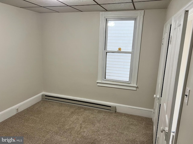 empty room with a drop ceiling, carpet, and a baseboard heating unit