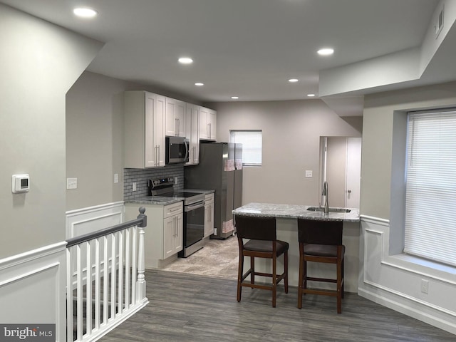 kitchen with light stone counters, appliances with stainless steel finishes, dark hardwood / wood-style flooring, sink, and white cabinets