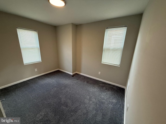 spare room featuring dark colored carpet and a wealth of natural light