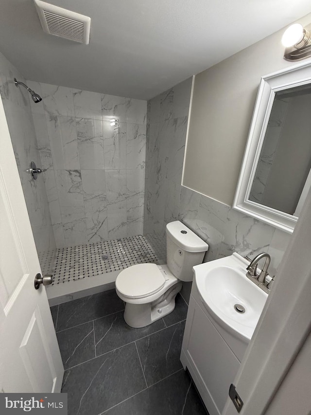 bathroom with toilet, tile walls, tile patterned flooring, a tile shower, and vanity