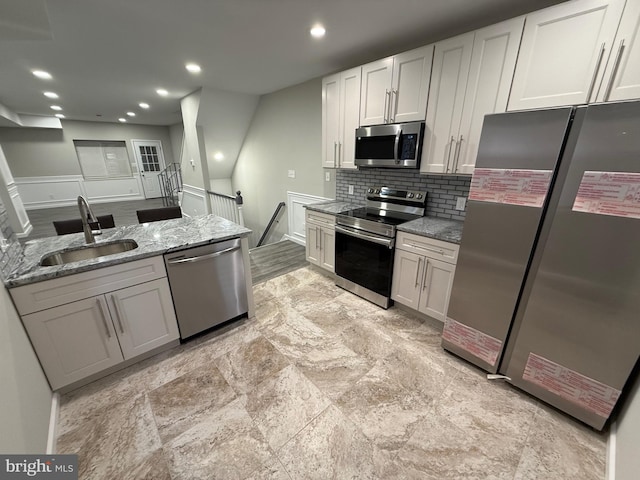 kitchen featuring stainless steel appliances, light stone counters, white cabinets, sink, and tasteful backsplash