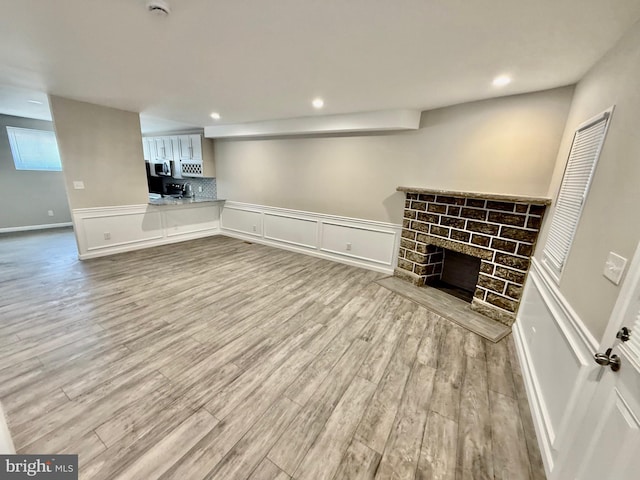 unfurnished living room featuring a stone fireplace and light wood-type flooring