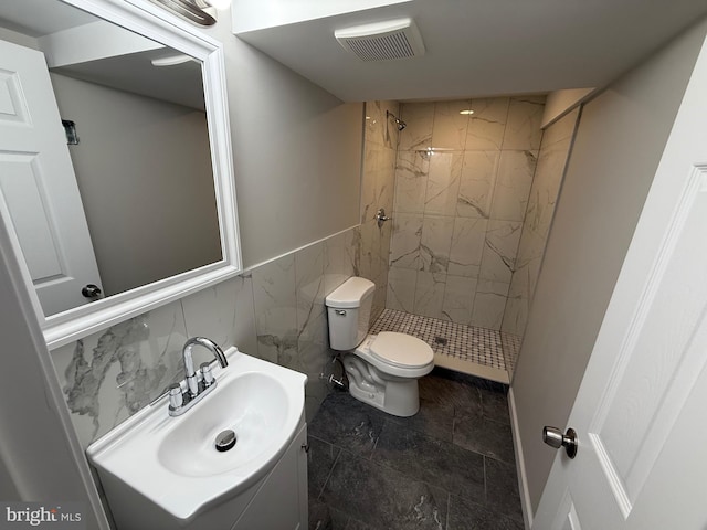 bathroom with a tile shower, vanity, toilet, and tile walls