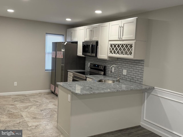 kitchen featuring kitchen peninsula, appliances with stainless steel finishes, light stone countertops, sink, and white cabinetry