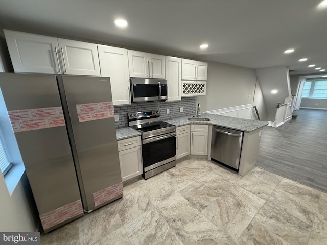 kitchen with sink, light stone countertops, white cabinetry, kitchen peninsula, and stainless steel appliances