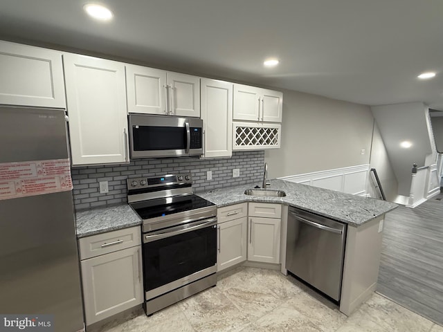 kitchen featuring white cabinetry, sink, light stone counters, kitchen peninsula, and appliances with stainless steel finishes