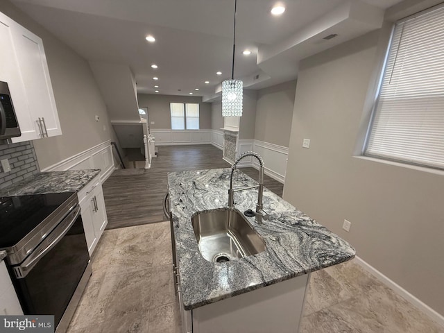 kitchen featuring white cabinets, decorative light fixtures, dark stone countertops, and a kitchen island with sink