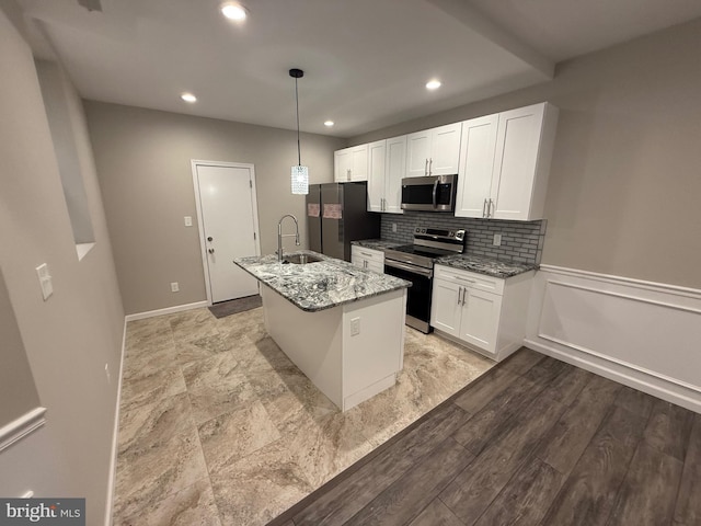 kitchen with light stone countertops, stainless steel appliances, a kitchen island with sink, sink, and white cabinets