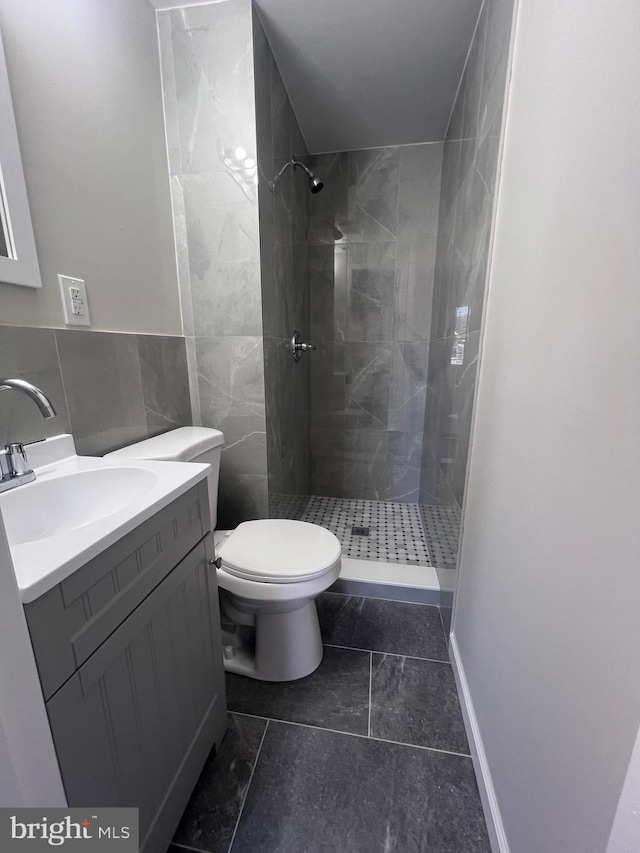 bathroom with vanity, tiled shower, tile walls, and toilet