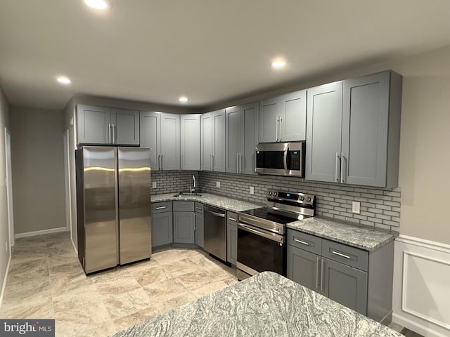 kitchen with gray cabinets, light stone countertops, appliances with stainless steel finishes, and tasteful backsplash