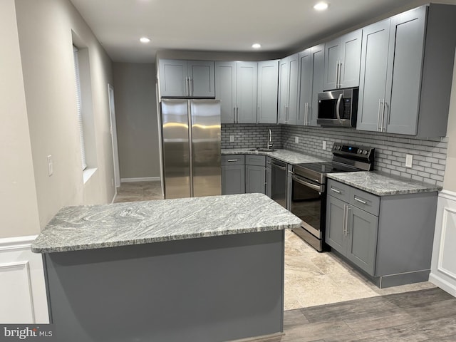 kitchen featuring light stone countertops, appliances with stainless steel finishes, light hardwood / wood-style floors, sink, and gray cabinets