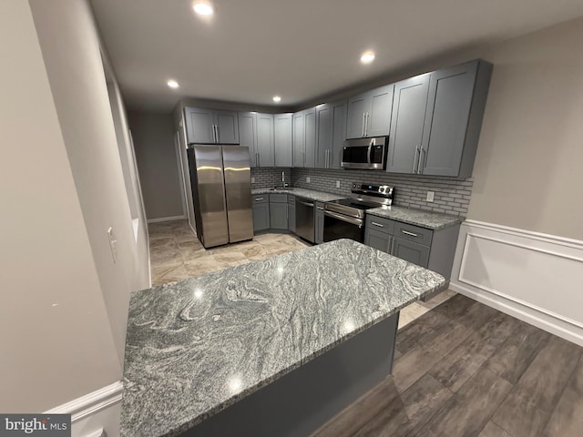 kitchen featuring appliances with stainless steel finishes, backsplash, light stone counters, and gray cabinetry