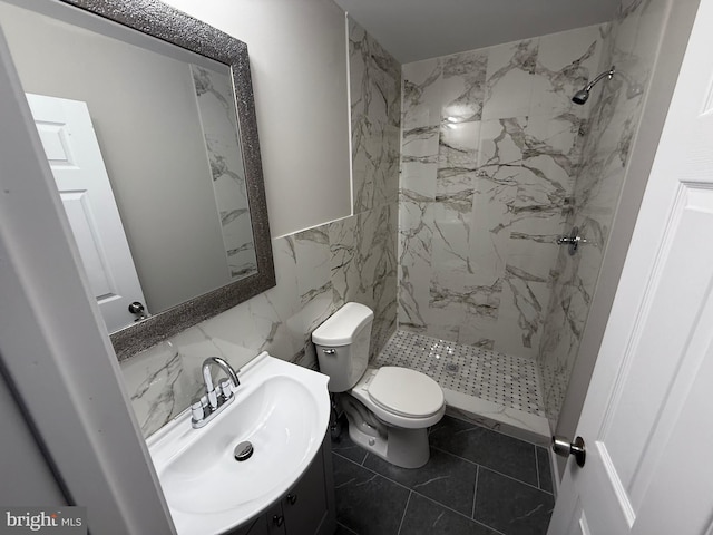 bathroom with tiled shower, vanity, toilet, and tile walls