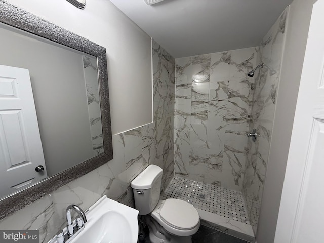 bathroom with sink, tiled shower, toilet, and tile walls