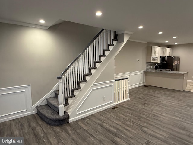 stairway with hardwood / wood-style floors, sink, and crown molding