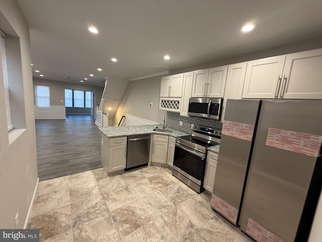 kitchen with kitchen peninsula, light stone counters, stainless steel appliances, sink, and white cabinets