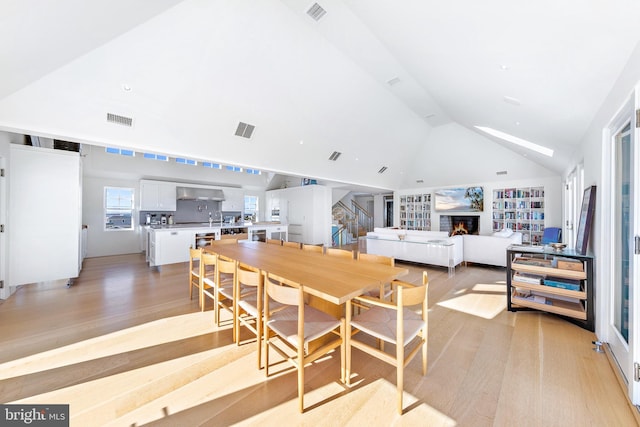 dining room with light wood-style flooring, visible vents, and vaulted ceiling