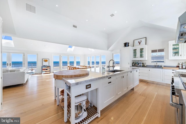 kitchen with sink, a center island with sink, light hardwood / wood-style flooring, a water view, and white cabinetry