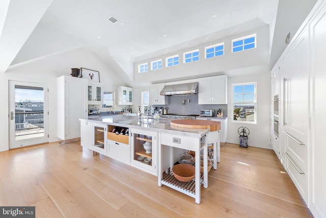 kitchen with a spacious island, high vaulted ceiling, light wood-style floors, and wall chimney range hood