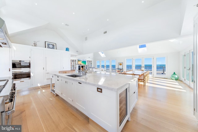 kitchen featuring light wood-style flooring, a large island with sink, a sink, white cabinetry, and high vaulted ceiling