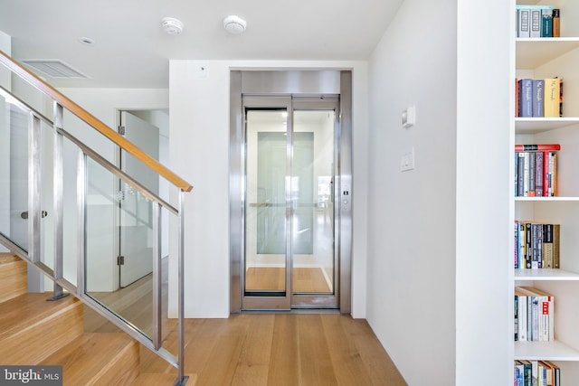 interior space with elevator, stairs, visible vents, and wood finished floors