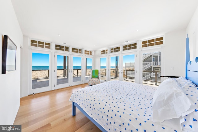 bedroom with a beach view, access to outside, a water view, and light hardwood / wood-style floors