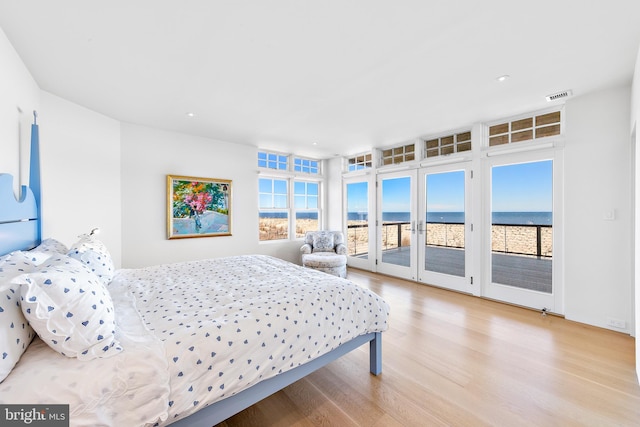 bedroom with access to exterior, light hardwood / wood-style flooring, and a water view