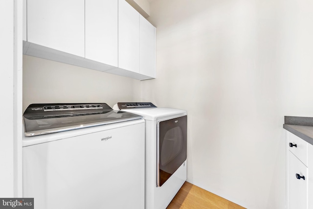 clothes washing area featuring cabinet space, light wood-style flooring, and washer and clothes dryer