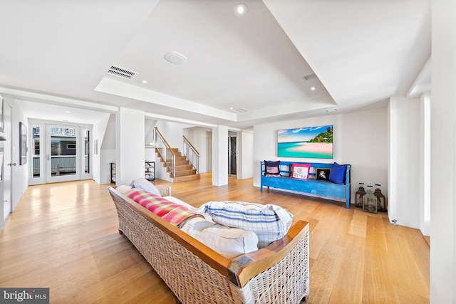 living room with visible vents, stairway, light wood-style floors, and a tray ceiling