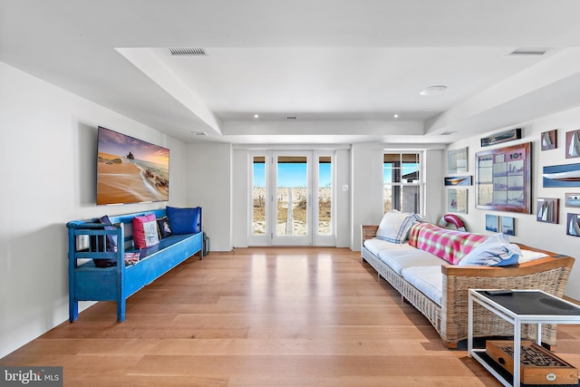 living room featuring visible vents, light wood-type flooring, and a raised ceiling