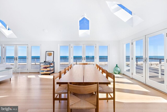 sunroom featuring lofted ceiling with skylight, french doors, a water view, and a view of the beach