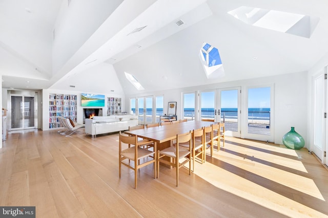 dining area featuring high vaulted ceiling, a skylight, a warm lit fireplace, and light wood-style flooring