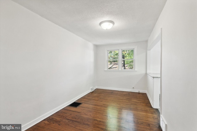 empty room with dark wood-type flooring and a textured ceiling