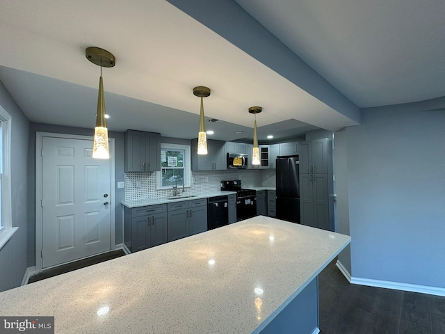 kitchen with tasteful backsplash, dark wood-type flooring, sink, black appliances, and hanging light fixtures