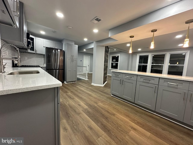 kitchen featuring stainless steel refrigerator, light stone countertops, gray cabinetry, dark hardwood / wood-style flooring, and pendant lighting