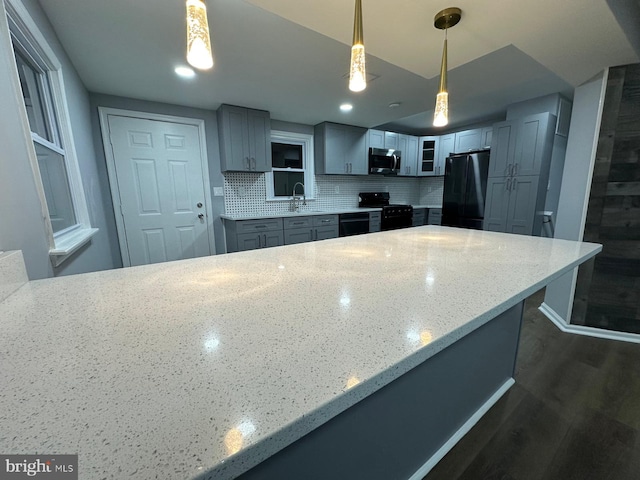 kitchen featuring light stone countertops, tasteful backsplash, dark wood-type flooring, black appliances, and decorative light fixtures