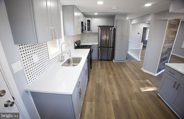 kitchen with gray cabinetry, sink, dark wood-type flooring, stainless steel appliances, and decorative backsplash