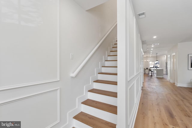 staircase with an inviting chandelier and wood-type flooring