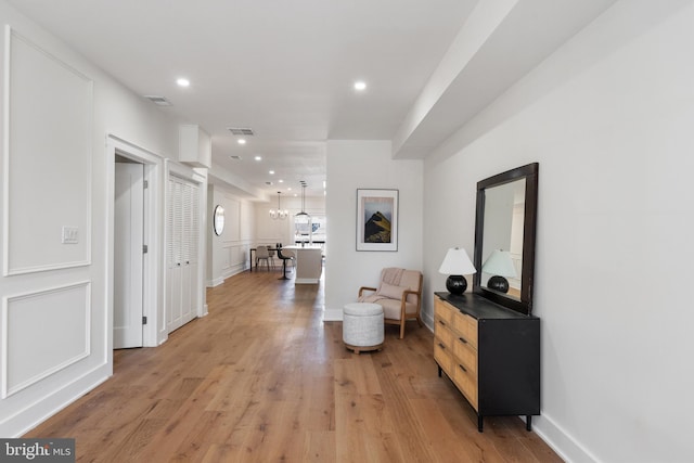 hallway with an inviting chandelier and light wood-type flooring