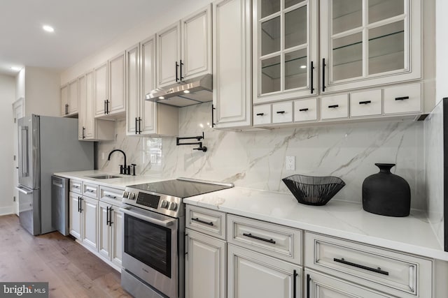 kitchen featuring tasteful backsplash, appliances with stainless steel finishes, sink, light wood-type flooring, and light stone counters