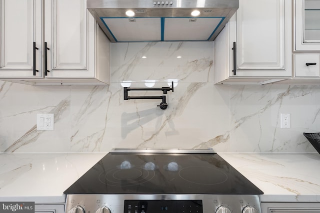 kitchen with black range, white cabinets, light stone counters, decorative backsplash, and ventilation hood