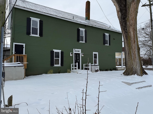 snow covered house featuring a chimney and metal roof