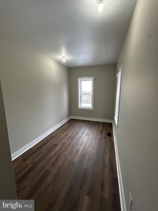 empty room featuring dark wood-style floors, visible vents, and baseboards