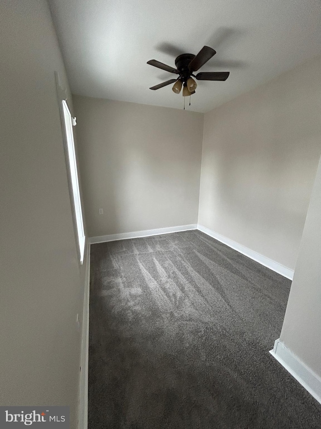 empty room featuring ceiling fan, baseboards, and dark colored carpet